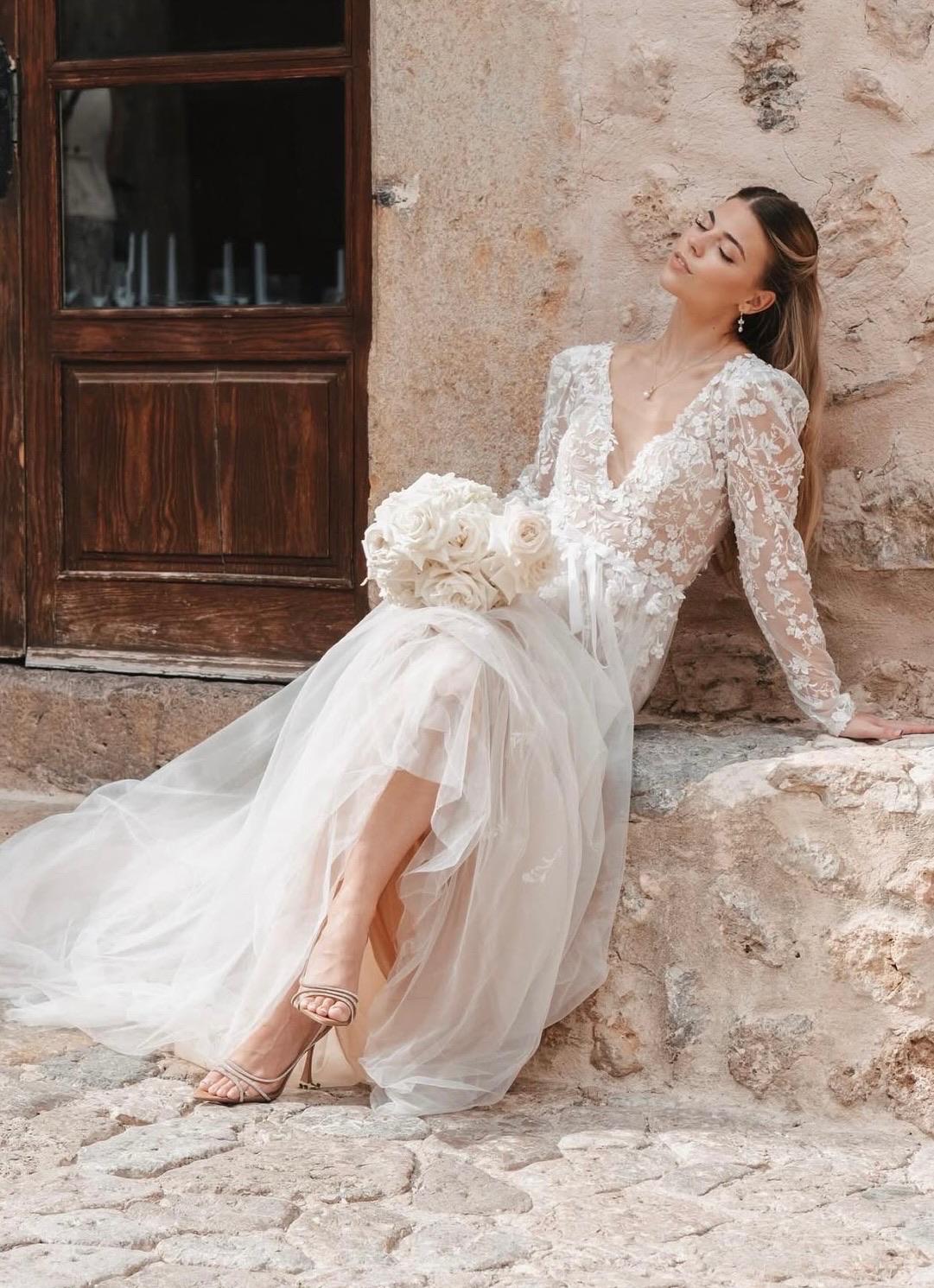 Braut in Spitzenkleid mit Brautstrauß auf Stein