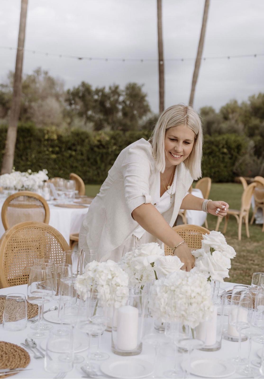 Katharina arrangiert weiße Blumen am gedeckten Hochzeitstisch